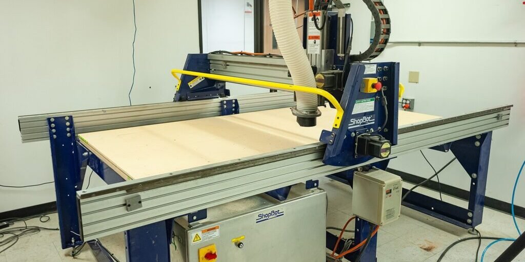 A ShopBot CNC router with a dust-collection hose sits ready on a shop floor.