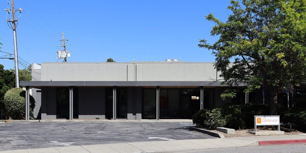 Low office building with a Y Combinator sign in the parking lot under a clear sky