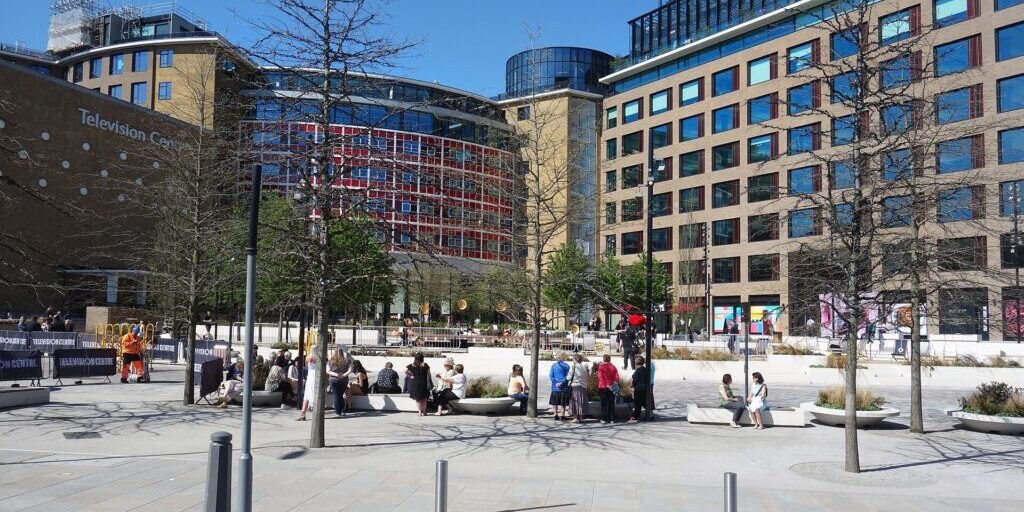Exterior plaza of Television Centre, a broadcasting building complex, on a sunny day with people walking outside